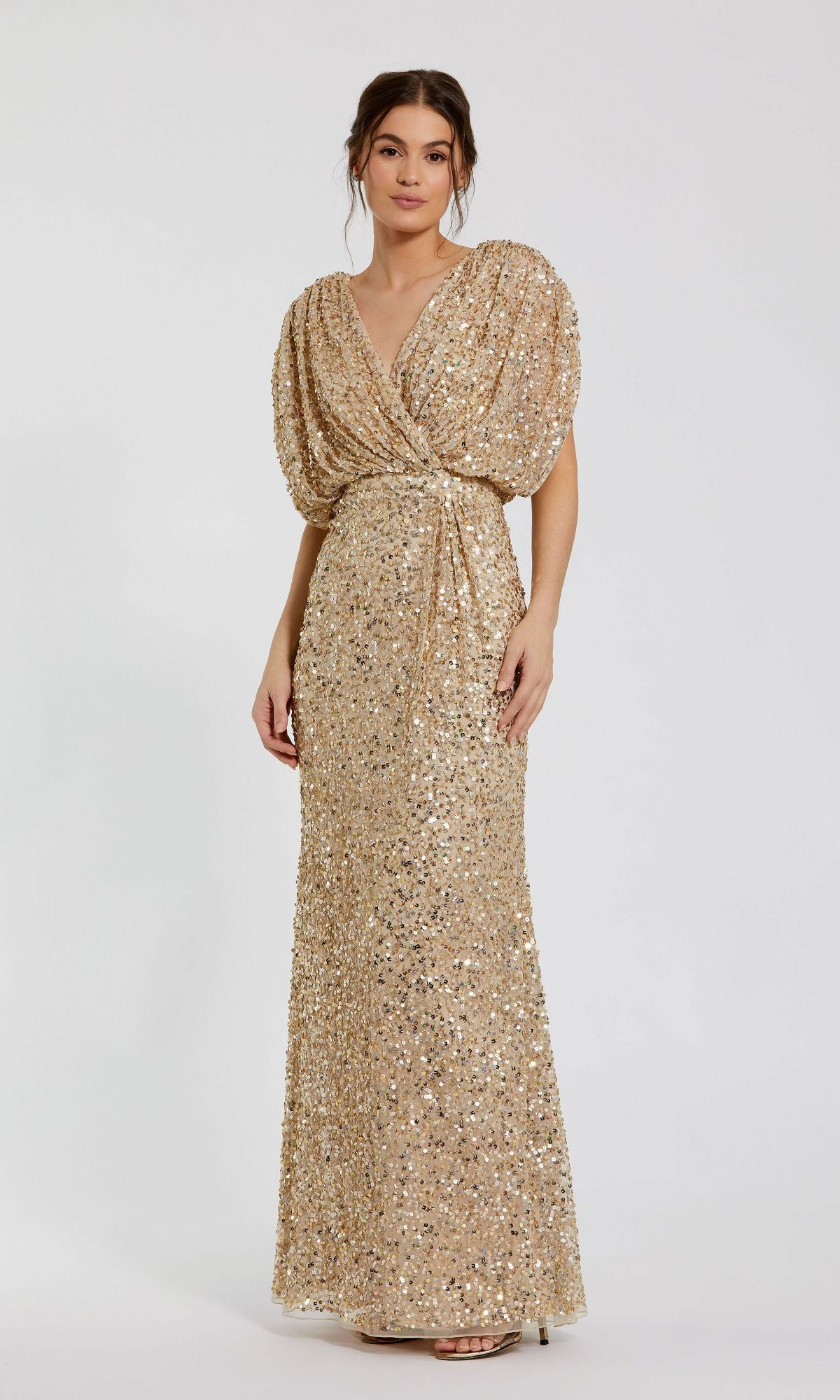 A woman stands against a plain white background wearing the Mac Duggal 5640: a floor-length gold sequin formal dress with short sleeves and a gathered waist.
